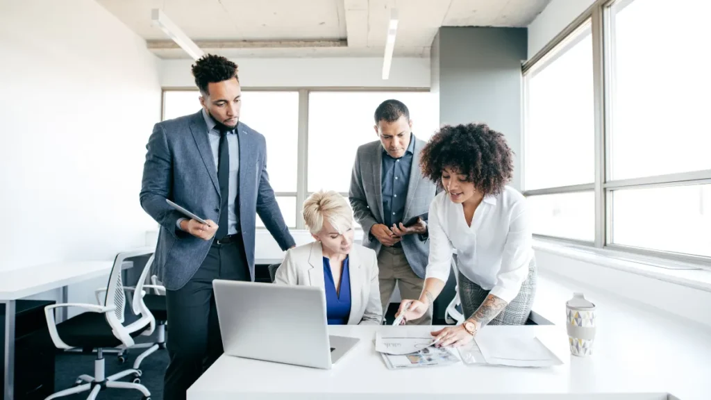 Diverse marketing team brainstorming around a laptop in a modern office, analyzing reports and planning social media strategy