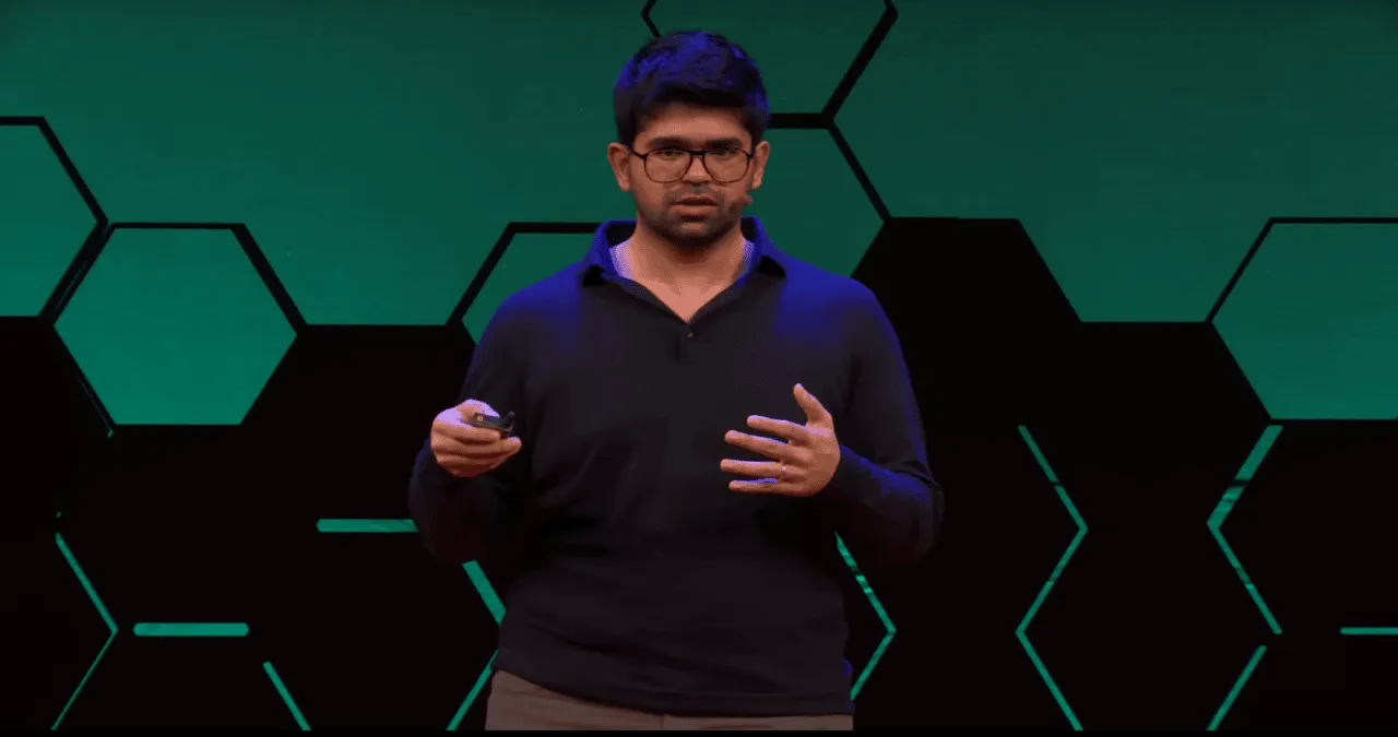 Arvind Srinivas, CEO of Perplexity, speaking on stage during a tech conference with a geometric green and black background.