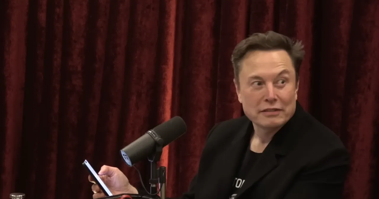 Elon Musk holding a phone during podcast interview, discussing future plans for xAI girlfriend app.
