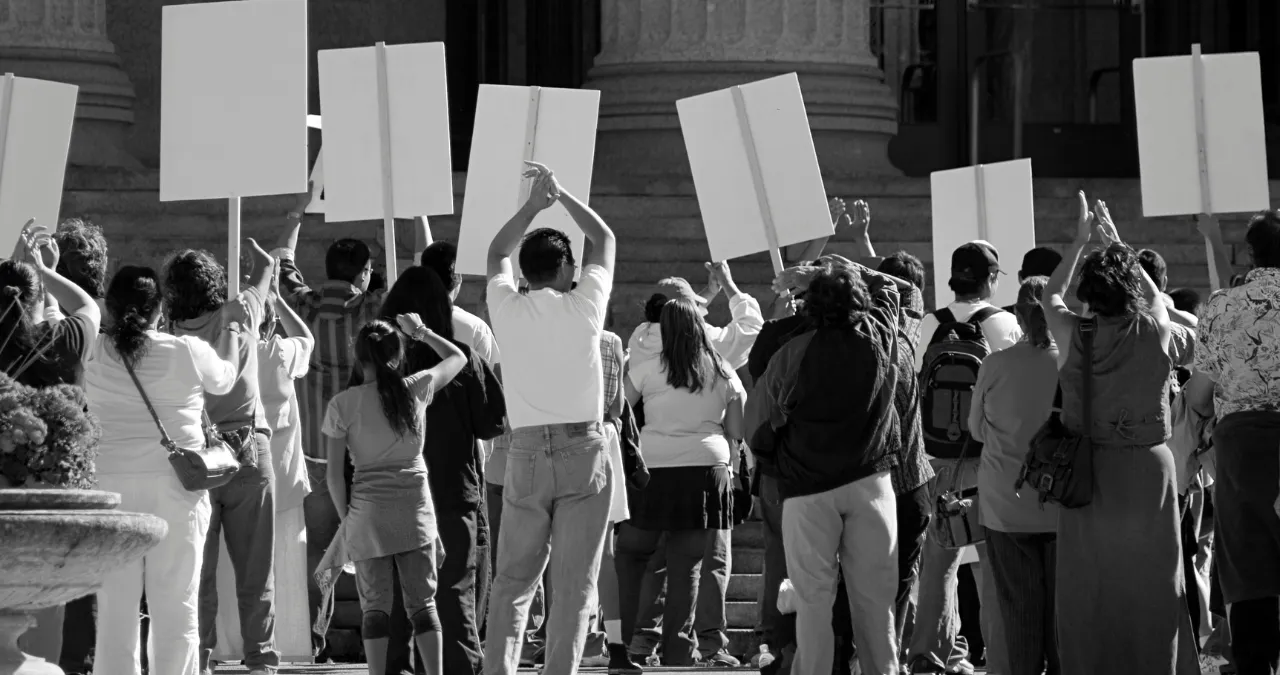 Crowd protesting with blank signs in front of building, symbolizing public backlash over AI girlfriend app controversy.